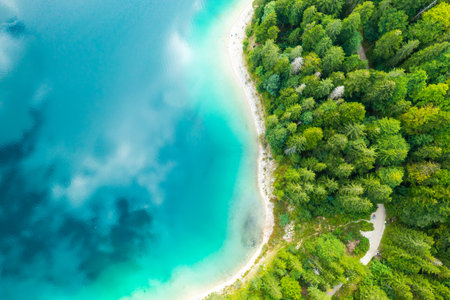Aerial view of a lake with turquoise water and clouds reflection and pine trees on the shore.の写真素材