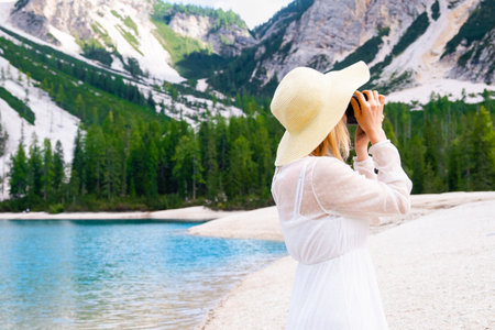 Blonde hair female photographer in straw hat and white dress taking pictures of Dolomites near Lake Braies with copy spaceの写真素材