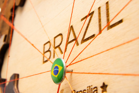 Brazil flag on the pushpin with red thread showed the paths of movement or areas of influence in the global economy on the wooden map. Planning of traveling or logistic concept. Network connection.の写真素材