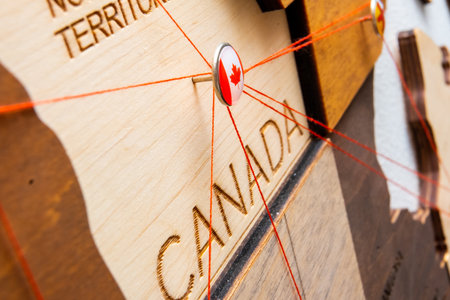 Canada flag on the pushpin and red threads on the wooden map. Travel or logistic routes. Influence in geopolitics and world economy.の写真素材