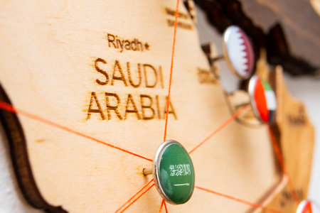 Saudi Arabia flag on the pushpin and red threads on the wooden map. Travel or logistic routes. Influence in geopolitics and world economy.の写真素材