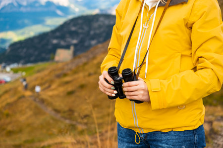 Close up a woman in a yellow jacket holding binoculars with mountains on the backgtound.の写真素材