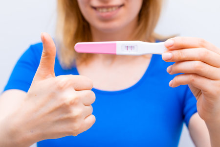 Smiling woman shows sign like and holding a positive pregnancy test.の写真素材