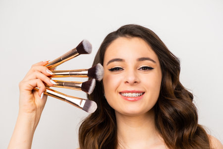 Portrait of young woman with a cosmetic brush near face on a grey background.の写真素材