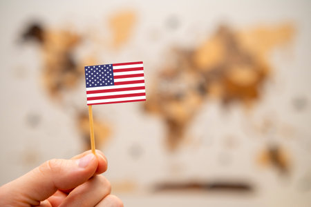 USA flag in mans hand on the wooden world map background. Global economy and geopolitics concept.の写真素材