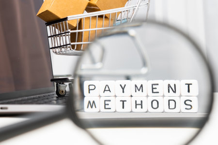 Payment methods on cubes through a magnifying glass, laptop and toy shopping cart on the background....