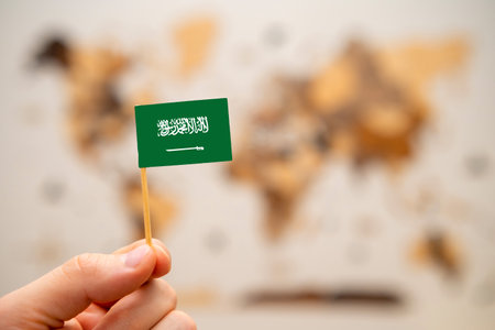 Saudi Arabia flag in mans hand on the wooden world map background. Global economy and geopolitics concept.の写真素材