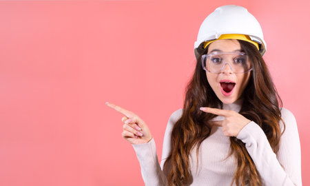 A surprised brunette in a helmet and glasses shows on the copy space on the pink backgroundの写真素材
