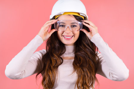 A surprised brunette in a helmet wears glasses on the pink background. Young happy architect.の写真素材
