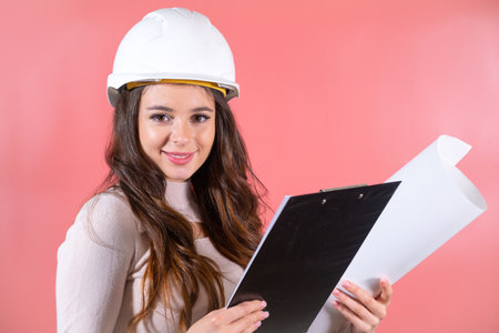 Smiling woman architect wearing white hardhat and and delighted expression enjoys jobの写真素材