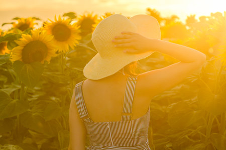 A young lady wearing a straw hat standing in the captivating sight of sunflowers.の写真素材