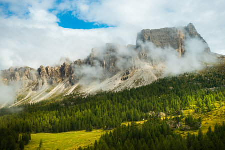 Stunning image of Rocky Dolomite Alps, where the lofty peak disappears into clouds with the forest at the mountains base.の写真素材