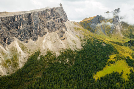 Stunning image of Rocky Dolomite Alps, where the lofty peak disappears into clouds with the forest...