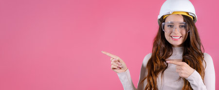 Young woman architect gleefully showcases the copy space on the pink background, her face lit up with happiness and enthusiasm.の写真素材