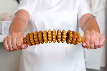 Wooden massager roller or handheld scrubbing wooden massager in therapist hands. Anti cellulite therapy and body care concept.の写真素材