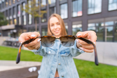 Young blonde woman holding eyeglasses standing near a modern building, view from first personの写真素材