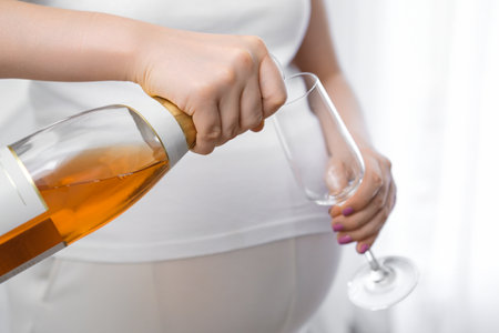 Pregnant woman pours an alcoholic drink into a glass. Negative effects of alcohol on the fetusの写真素材