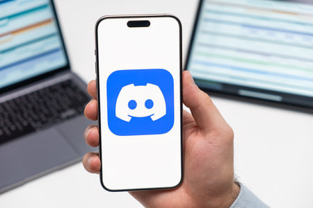 Discord logo of social media application on the screen of smart phone in mans hand, laptop and tablet on the background, December 2023, Prague, Czech Republicのeditorial素材