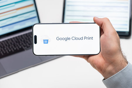 Google Cloud Print application logo on the screen of smart phone in mans hand, laptop and tablet are on the table in the background, December 2023, Prague, Czech Republicのeditorial素材
