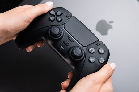 BERLIN , GERMANY - FEBRUARY 14 2024: Womans hands holding video game controller over MacBook Proのeditorial素材