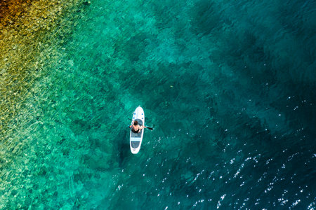 Top view of a woman moving through the sea with clear water, sitting on a paddle board.の写真素材