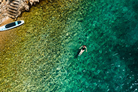 Woman swimming on the back in crystal clear water and paddle board is on the seaside.の写真素材