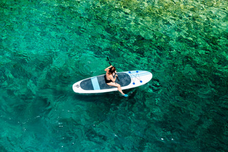 Woman paddling near the rocky seaside using paddle board or SUP.