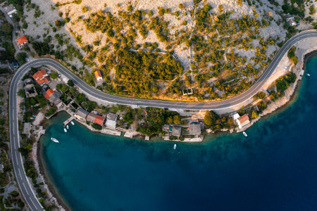 Aerial view of a coastal village with winding road and clear blue water in the afternoon sun.の写真素材