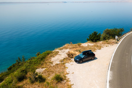 Car with a roof box, parked near a scenic cliffside road, overlooking a vast and azure sea.の写真素材