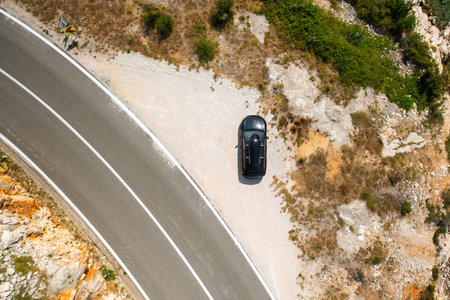 Top view of black car with a roof box, parked on a wide cliffside road.の写真素材