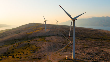 Wind turbines generate eco-friendly power on Pag Island, encircled by the Adriatic Sea at sunset.の写真素材