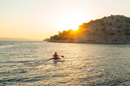 Man in orange vest navigating on the paddleboard in the sea at sunset.の写真素材