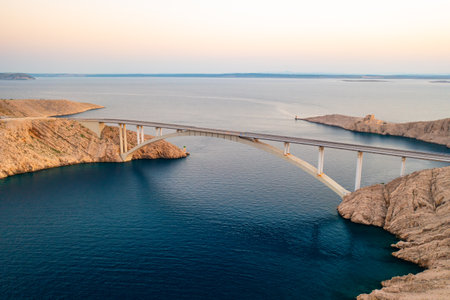 Pag Bridge with driving vehicles lasts over Adriatic sea channel. Vital infrastructure creates interest among tourists offering stunning viewsの写真素材