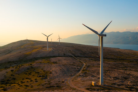 Wind turbines generate eco-friendly power on Pag Island, encircled by the Adriatic Sea at sunset.の写真素材