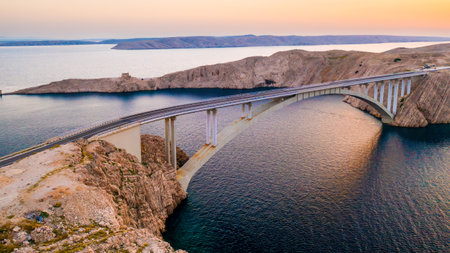 Pag Bridge with driving vehicles over Adriatic Sea channel at sunset. Road network connects island to Croatian mainland offering stunning viewsの写真素材