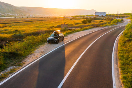 A car parked beside a tranquil river on a winding road during golden hour in the countryside.の写真素材