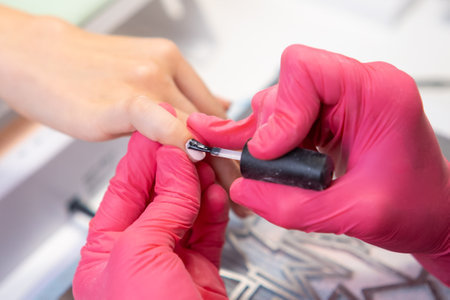 Manicurist applies the top layer of the gel polish for the client in a modern salon.