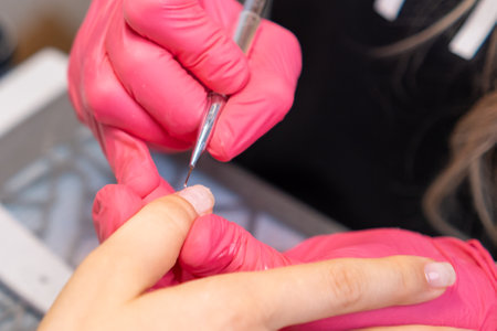 Experienced nail technician applying base coat before gel polish manicure in a salonの写真素材