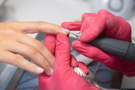 Nail technician uses a nail drill to provide a hardware manicure for a client in a salon.の写真素材