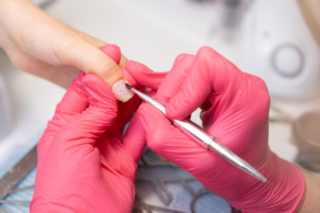 Manicurist applies a base coat of gel polish on woman fingernail using a brush in beauty salon.の写真素材