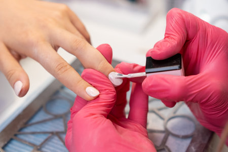 Skilled nail technician in pink gloves carefully paints gel polish on a womans nails in a cozy salonの写真素材