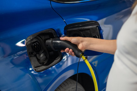 Woman connects a charging cable to an electric car in a public parking area