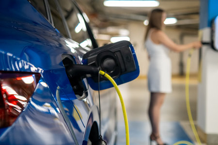 Electric car charging in a parking garage, while woman paying for charging.