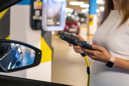 Electric vehicle charging process in a modern parking garage by woman.の写真素材