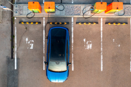 Top view of blue electric car receives electricity at public charging point. Parking lot equipped with plugs and connectors for quick replenishing of energyの写真素材