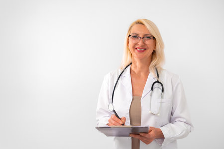 Confident female therapist, blonde, wearing white lab coat and stethoscope, standing on white background with empty space for text. Healthcare and medical professional concept.の写真素材