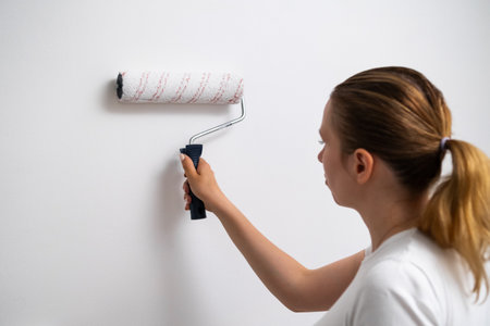 Woman holding a paint roller, painting a white wall home, renovation close up