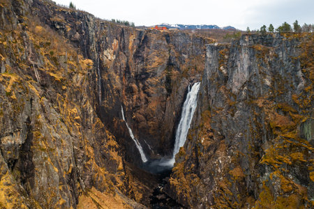 Voringsfossen waterfall with powerful stream cascading down deep gorge framed by imposing barren cliffs. Distant mountain under sky in Norwayの写真素材