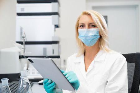 Blonde woman wearing a protective lab mask and gloves writing results of chemical experiments on a...
