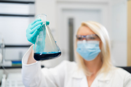 Blonde woman scientist in lab observing liquid solution in glass flask